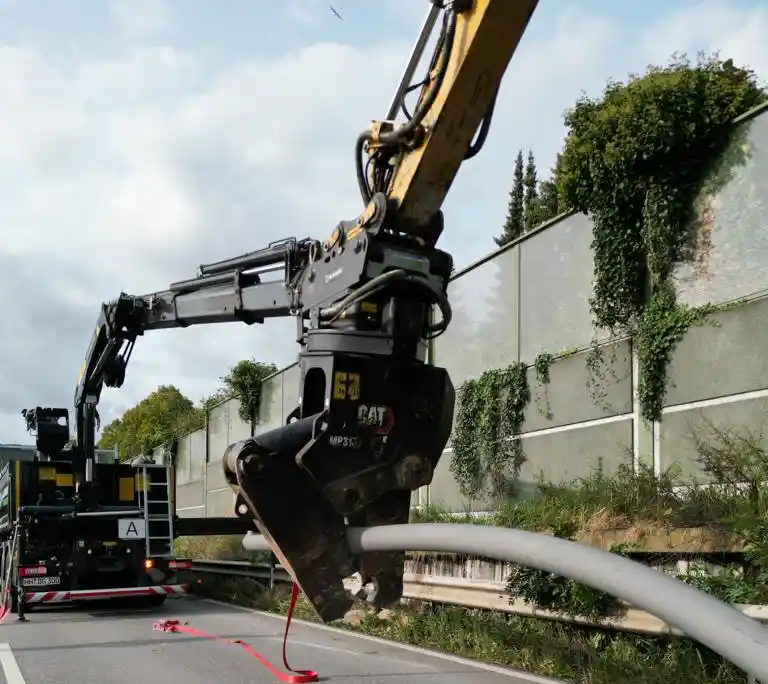 Greiferarm hebt Metallrohr bei Straßenarbeiten